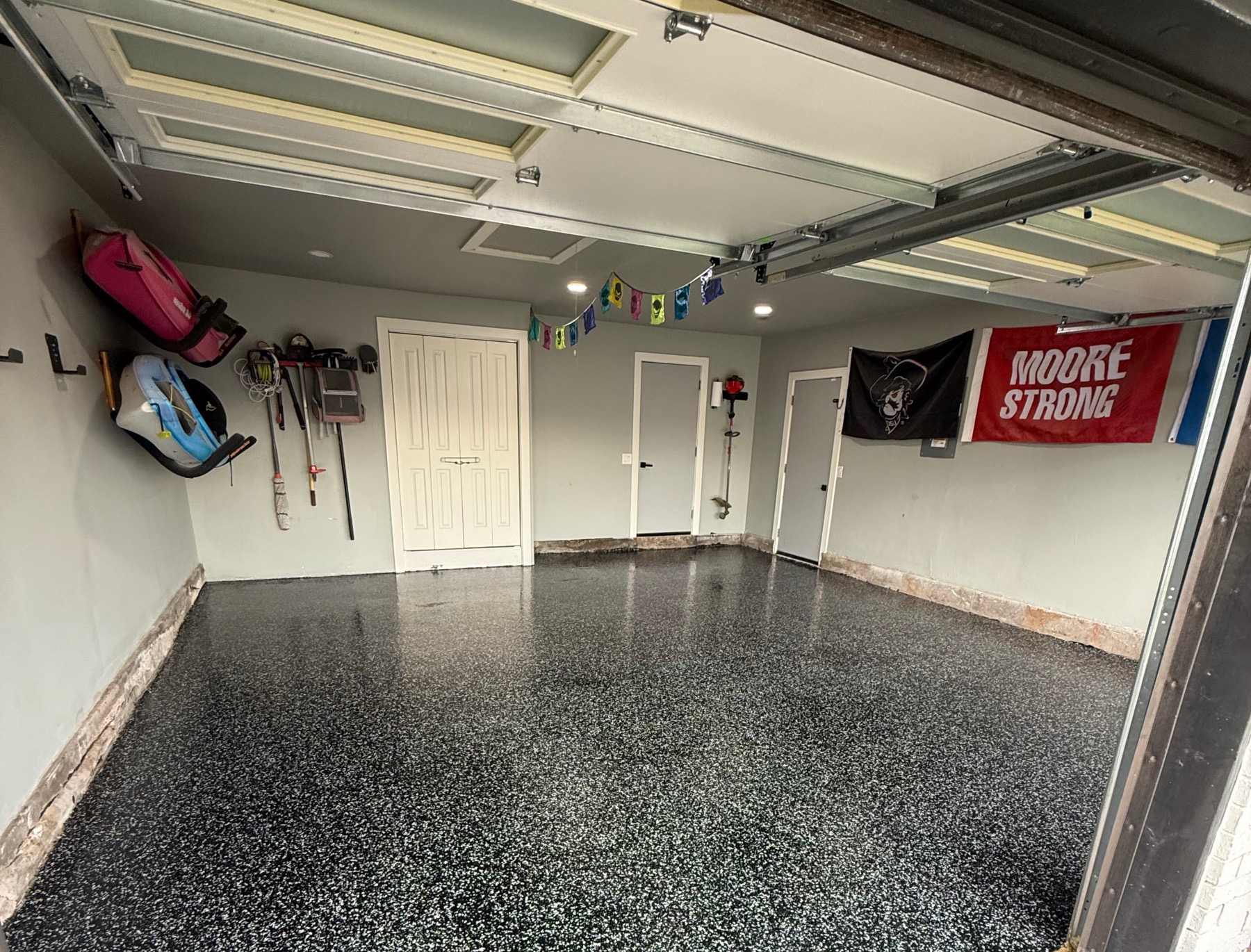 Finished two-car garage floor with black base, Raven Torginol flake and polyaspartic topcoat, seen from the open garage door